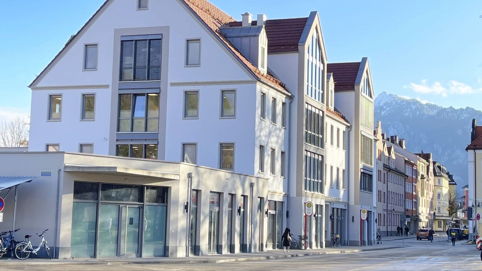 Picturesque street featuring modern architecture with a serene mountain backdrop on a sunny day.